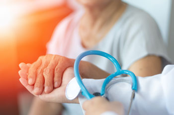 Picture of a Physician holding a stethoscope in one hand and an elderly female patients hand in the other.