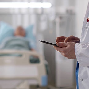 Picture of a male patient lying down in a swing bed and male Physician at the end up the bed wearing a medical coat and holding a smart phone in his hand.